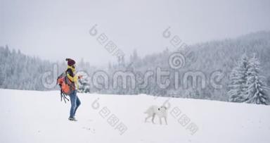 年轻的游客拿着一个橙色的袋子在雪田的中间，走在一只白色的狗旁边，游客拿着一只橙色的袋子。